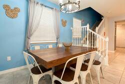 Gather in a bright dining area with a wooden table, white chairs, blue accent walls, soft curtains, modern chandelier, and staircase nearby, perfect for family meals during vacation.