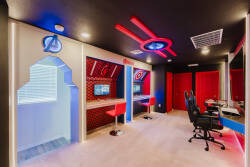 Enter our vibrant game room with sleek black walls and bold red lighting. Two modern workstations adorned with illuminated superhero designs provide the perfect mix of excitement and relaxation for gaming or creative pursuits.