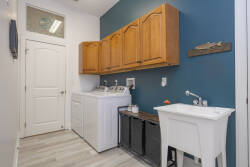 Discover a practical laundry room with rich wooden cabinets and a vibrant teal accent wall. This well-organized space features modern appliances and a handy utility sink, ensuring a functional experience during your stay.
