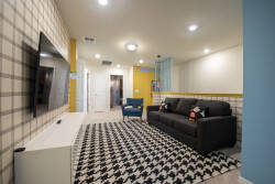 Welcome to a vibrant living room with a striking black-and-white rug and a sleek black sofa adorned with colorful pillows. The bright yellow accent wall and playful blue decor create a lively atmosphere perfect for relaxation.