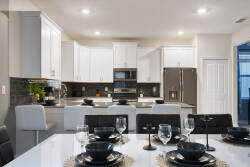 Welcome to a stylish kitchen with sleek white cabinetry and a warm gray backsplash. The modern dining table, elegantly set with black dishware, invites you to share meals and laughter in this inviting culinary space.