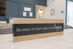 A stylish wooden sign reading "Do more of what makes you happy" welcomes you to this beautifully decorated room, where warm wood tones complement the deep blue wall, creating a cozy and inviting atmosphere.