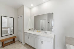 Freshen up in a bright bathroom with a double vanity, large mirror, white cabinetry, clean counters, soft lighting, a wooden bench, and calm neutral finishes
