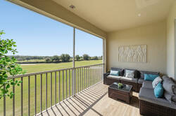 Relax on a covered balcony with cozy outdoor seating, sliding glass doors, wood-style flooring, and peaceful green views, creating a comfortable space to enjoy fresh air and quiet moments.