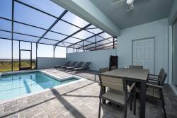 Experience relaxation in this sunlit covered patio, featuring a sleek dining set and lounge chairs beside the private pool. The cool, textured pavers seamlessly blend indoor and outdoor living, inviting you to unwind in style.