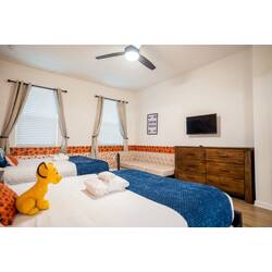Rest in a bright safari-themed bedroom with two cozy beds, blue accents, soft curtains, a wall-mounted TV, and a comfortable seating area. Playful details and warm wood floors create a relaxing space for family vacation.