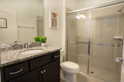 Step into this chic bathroom, featuring sleek granite countertops and modern dark cabinetry that beautifully contrasts with the light tile. The glass-enclosed shower adds a touch of luxury, ensuring a refreshing start to your day.