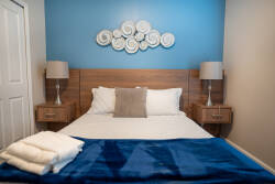 The calming blue accent wall beautifully contrasts with the warm wood furniture, creating a cozy atmosphere. With plush bedding and stylish lamps flanking the bed, this room invites restful nights and rejuvenating mornings.