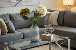A sleek glass coffee table complements the plush gray sofa adorned with soft, textured pillows, creating a cozy yet stylish atmosphere. A tasteful vase of fresh flowers adds a vibrant touch, inviting relaxation and conversation.