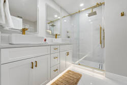 This stylish bathroom features sleek white cabinetry and chic gold fixtures for a vibrant atmosphere. Enjoy the spacious glass-enclosed shower, dual sinks, and ample lighting that enhance the modern design for your comfort.