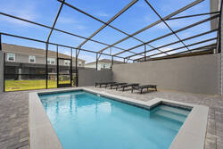 Relax in a private screened pool area with clear blue water, lounge chairs, paved deck, privacy walls, and open sky views, creating a refreshing space for family vacation moments.