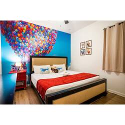 Rest in a cheerful balloon-themed bedroom with a cozy king bed, bright blue mural wall, red accents, and playful framed art. Soft lighting, warm wood floors, and simple decor create a fun and comfortable space to unwind.
