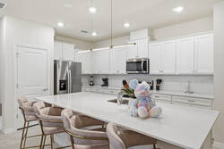 Cook and gather in a bright modern kitchen with white cabinets, stainless steel appliances, a spacious island, soft pendant lighting, plush bar chairs, and playful Mickey decor, perfect for family meals during vacation.