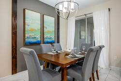 Join us at the chic wooden table, where plush gray chairs invite conversation over shared meals. Soft natural light filters through sheer curtains, and ocean-themed artwork enhances the elegant decor, creating a warm atmosphere.