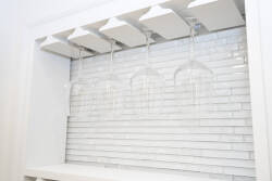 This stylish kitchen, with its chic white tile backsplash and minimalist glassware rack, combines sleek design and functionality, creating an inviting space perfect for gathering and indulging in your culinary creativity.