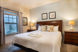 This bright and airy bedroom boasts a plush king-sized bed with decorative pillows, inviting you to relax. Soft natural light pours in, highlighting tasteful artwork and warm bedside lamps that create a cozy atmosphere.