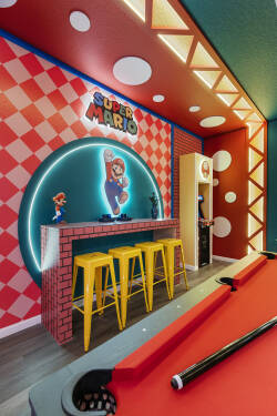 Play in a colorful Super Mario game room with a pool table, arcade machine, fun wall art, bright lighting, and bar stools, creating a lively space for family entertainment during vacation.
