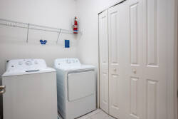 Take care of laundry with ease in a clean laundry room featuring a washer, dryer, storage closet, and wall shelf. Bright lighting and a simple layout make it a practical space for keeping clothes fresh during vacation.