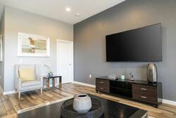 Enjoy a thoughtfully designed living area with a sleek large-screen TV on a soft gray wall. The warm wood flooring pairs perfectly with modern furnishings like a stylish chair and chic coffee table, creating a cozy atmosphere.