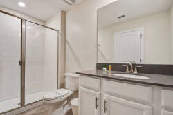 This bright bathroom features sleek dark countertops and crisp white cabinetry for a fresh vibe. The spacious glass shower offers a refreshing start or end to your day, while the ample lighting enhances the airy atmosphere.