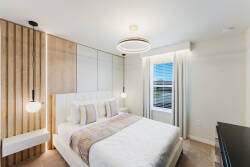 This cozy bedroom features a plush bed flanked by stylish pendant lights, creating a warm ambiance. The wooden accent wall adds a touch of natural texture, while large windows invite soft, natural light to brighten the space.