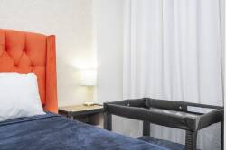 The vibrant orange headboard brightens this cozy bedroom, while soft blue bedding invites relaxation. Natural light streams through sheer curtains, creating a warm atmosphere ideal for restful nights.
