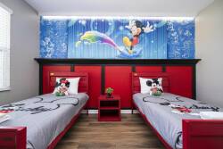 Bright and playful, this vibrant bedroom features two twin beds with bold red frames, complemented by cheerful Mickey Mouse bedding. The colorful wall mural adds a whimsical touch, creating a fun atmosphere for guests of all ages.