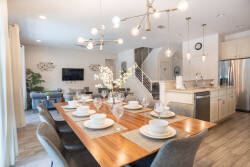 Enjoy a delightful meal at the stunning wooden dining table, set with elegant dishware. The soft lighting and open layout create a warm atmosphere, while the sleek kitchen and modern decor enhance the inviting experience.