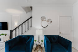Relax in a chic sitting area with luxurious navy blue velvet chairs. Bright white walls and modern decor create an inviting atmosphere, while stylish light fixtures and elegant mirrors enhance the sophisticated vibe.