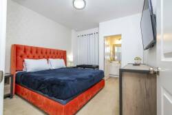 Welcome to a cozy bedroom with a vibrant orange tufted headboard and soft gray walls. Relax on plush navy bedding as natural light filters through the curtains, creating a serene and inviting atmosphere for your stay.