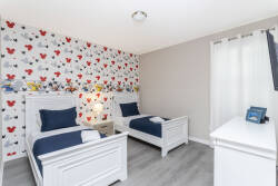 This charming bedroom features two twin beds with crisp white frames and colorful floral wallpaper, creating a bright and playful atmosphere. Sheer curtains let in light, making the space feel even more inviting for your stay.