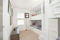 This bright and cozy room boasts a playful white bunk bed and warm beige carpeting. Cheerful artwork decorates the walls, and natural light flows through the windows, creating a welcoming and cheerful atmosphere for guests.
