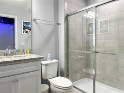 Freshen up in a clean bathroom with a glass shower, granite vanity, large mirror, white cabinets, soft lighting, and neutral tones, offering comfort and convenience during vacation.