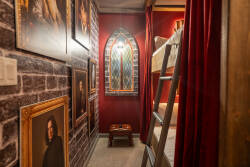 Step into a unique hallway showcasing rich red walls adorned with intriguing portraits, creating a captivating backdrop. A charming stained glass window adds a touch of warmth, while a cozy lofted bunk beckons for restful nights.