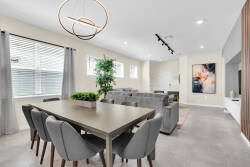 Bright and airy, this dining area features a sleek table surrounded by plush gray chairs, creating a fine spot for meals and gatherings. Large windows invite natural light, while a stylish chandelier adds a contemporary touch.