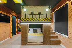 Experience a playful haven with a unique bunk bed design adorned in cheerful yellow accents and fun graphics. Enjoy restful nights in cozy layered bedding, enhanced by warm wood textures for added comfort and style.