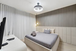Rest in a modern bedroom with a cozy bed, padded headboard, vertical accent wall, soft lighting, full curtains, TV, and a calm neutral design, creating a comfortable retreat during your vacation.