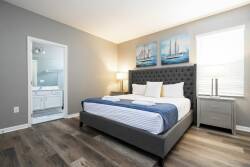 Enjoy a stylish bedroom with a plush gray upholstered headboard and crisp white linens, enhanced by charming nautical-themed artwork. Natural light fills the space, offering a bright and airy ambiance for your stay.