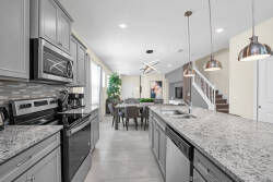 Enjoy a bright, modern kitchen with stylish gray cabinets and stunning granite countertops that inspire culinary creativity. Warm pendant lighting over the spacious island creates an inviting space for shared meals in the dining.