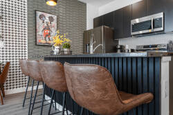 Welcome to a chic kitchen featuring rich leather bar stools and a sleek black countertop, perfect for your morning coffee. With eye-catching artwork and a vibrant patterned wall, this space is both functional and stylish.