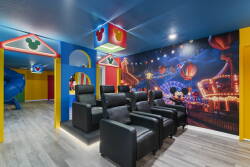 Step into a vibrant entertainment room with plush black reclining seats that invite relaxation. Colorful accents and a whimsical wall mural create a playful atmosphere, perfect for movie nights or enjoying time with loved ones.