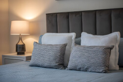 Enjoy peaceful nights in this beautifully styled bedroom with a plush upholstered headboard and soft bedding. The warm bedside lamp enhances the serene color palette, offering a cozy and inviting atmosphere for your stay.