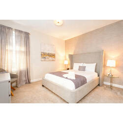 Rest in a bright and cozy bedroom with a comfortable bed, soft white bedding, gray accents, elegant headboard, bedside lamps, neutral curtains, carpeted floor, and warm decor.