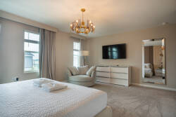 Enjoy comfort in this spacious bedroom with plush carpet, soft beige walls, and a stylish chandelier. Relax in the cozy seating area and bask in the natural light from large windows that create a modern, inviting atmosphere.