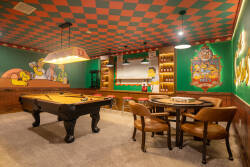 Step into a vibrant game room that captures the spirit of fun, featuring a classic pool table and colorful checkered ceiling. Bold murals bring character to the walls, while cozy seating invites friendly competition and laughter.