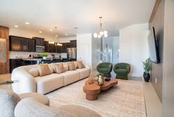 Relax in a bright open living area with a large sofa, green accent chairs, wall-mounted TV, modern lighting, and a nearby kitchen, creating a comfortable space to gather during your vacation.