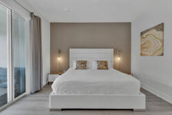 Experience restful nights in this well-appointed bedroom, featuring a sleek white bed framed by soothing earthy tones. Soft lighting highlights the chic wall art, while large windows invite natural light and fresh air.