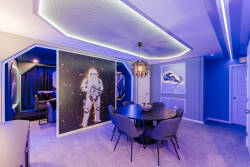 Enter a vibrant dining area bathed in soft blue light, featuring a stylish round table perfect for gatherings. The whimsical astronaut mural adds charm, while cozy seating guarantees comfort during every delightful meal shared.