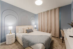 This cozy bedroom, with soft blue walls and elegant arches, creates a tranquil atmosphere. Experience restful nights on plush bedding, paired with stylish nightstands and gently draped curtains for added warmth and sophistication.