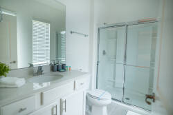 Experience a bright, airy bathroom with sleek glass shower doors and a spacious vanity featuring a stunning countertop. Natural light flows through the modern window, creating a crisp, clean design that enhances your comfort.